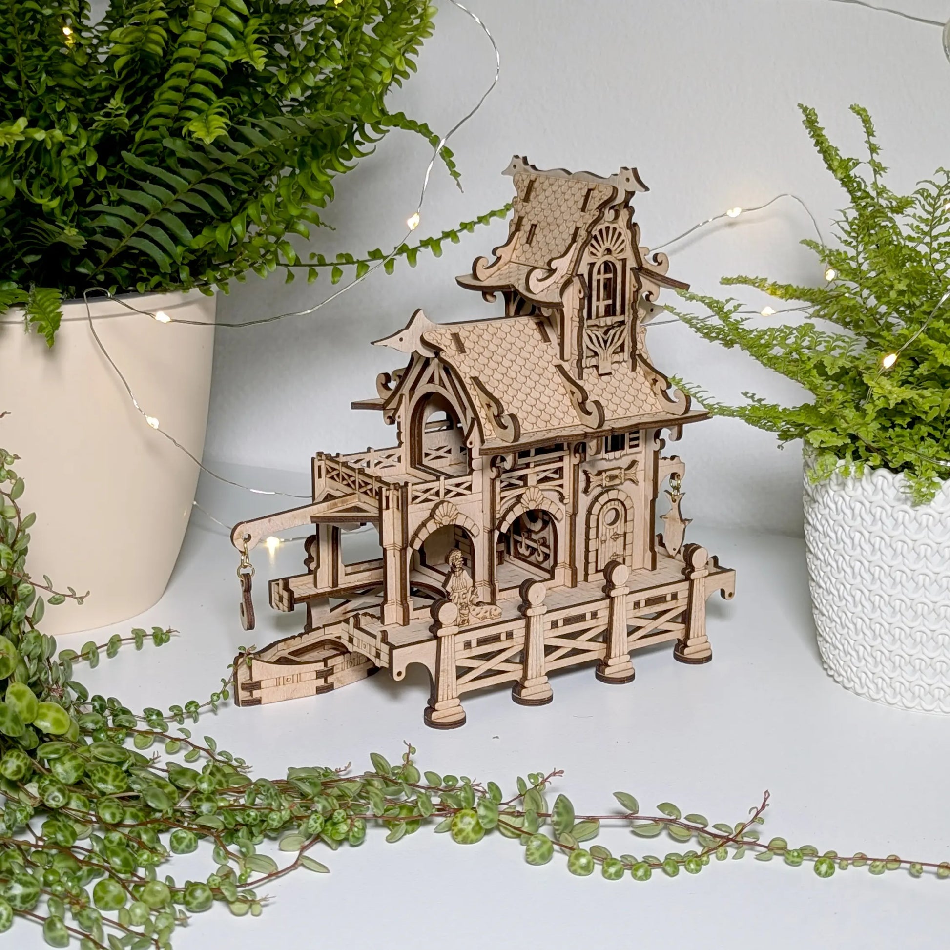 Atmospheric product photography of a 3D miniature lighthouse puzzle styled near flowers with laser cut plywood.