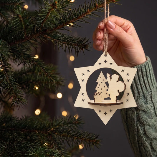 Hand hangs 3D laser cut plywood star bauble with slotted Santa, pine tree, and gift on a glowing Christmas tree.