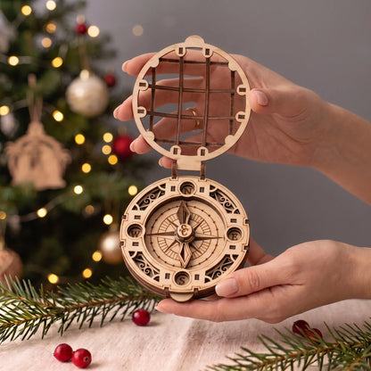 Hands hold open laser cut plywood Santa Claus compass toy showing true scale against a glowing Christmas tree.