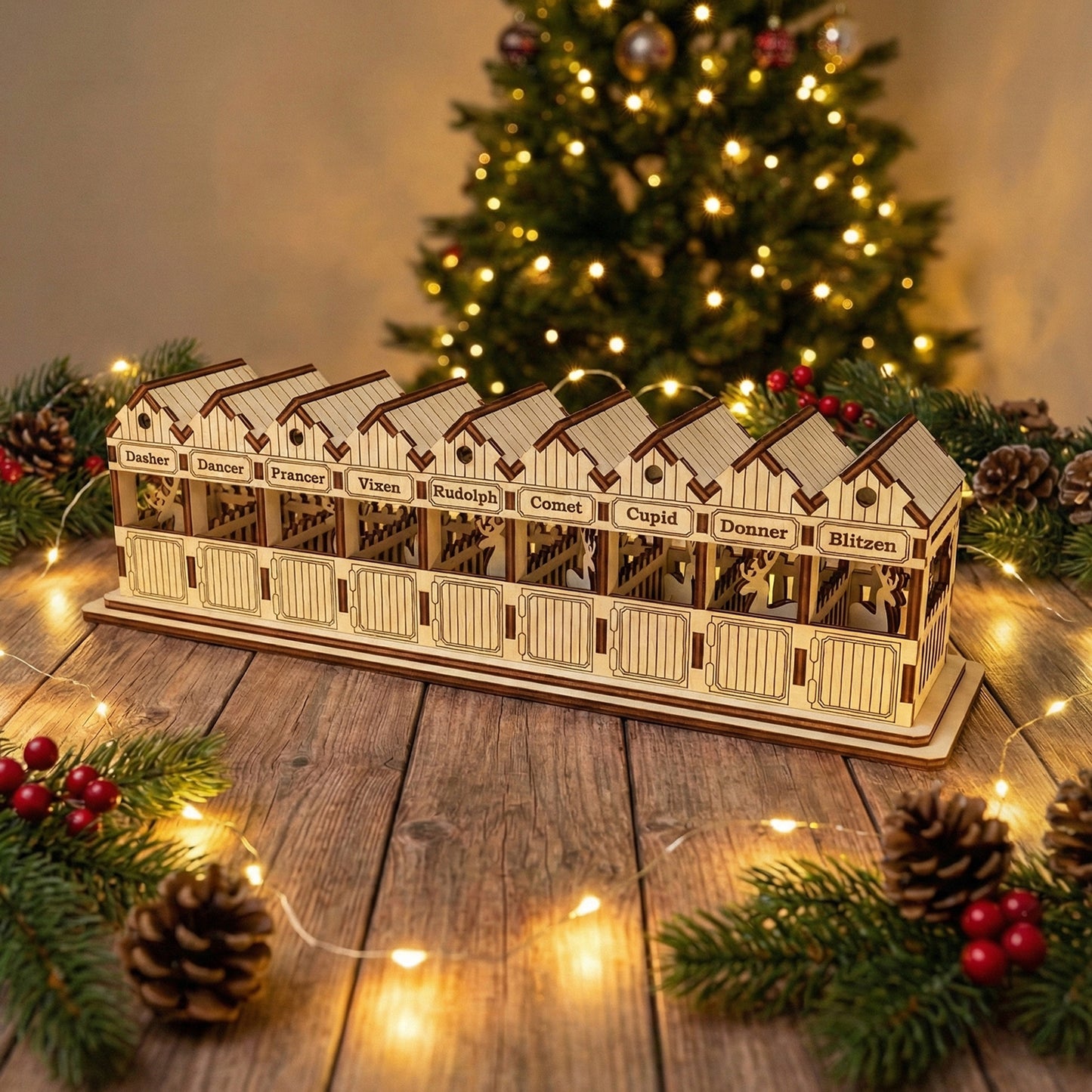 Detailed laser cut wooden Santa's Reindeer barn featuring cutout reindeer silhouettes in each named stall from Dasher to Blitzen, displayed in front of a twinkling holiday tree background.