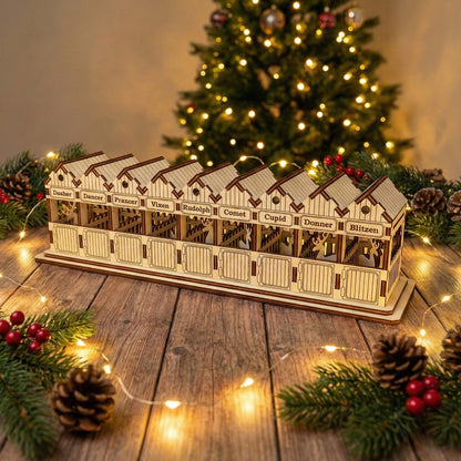 Detailed laser cut wooden Santa's Reindeer barn featuring cutout reindeer silhouettes in each named stall from Dasher to Blitzen, displayed in front of a twinkling holiday tree background.