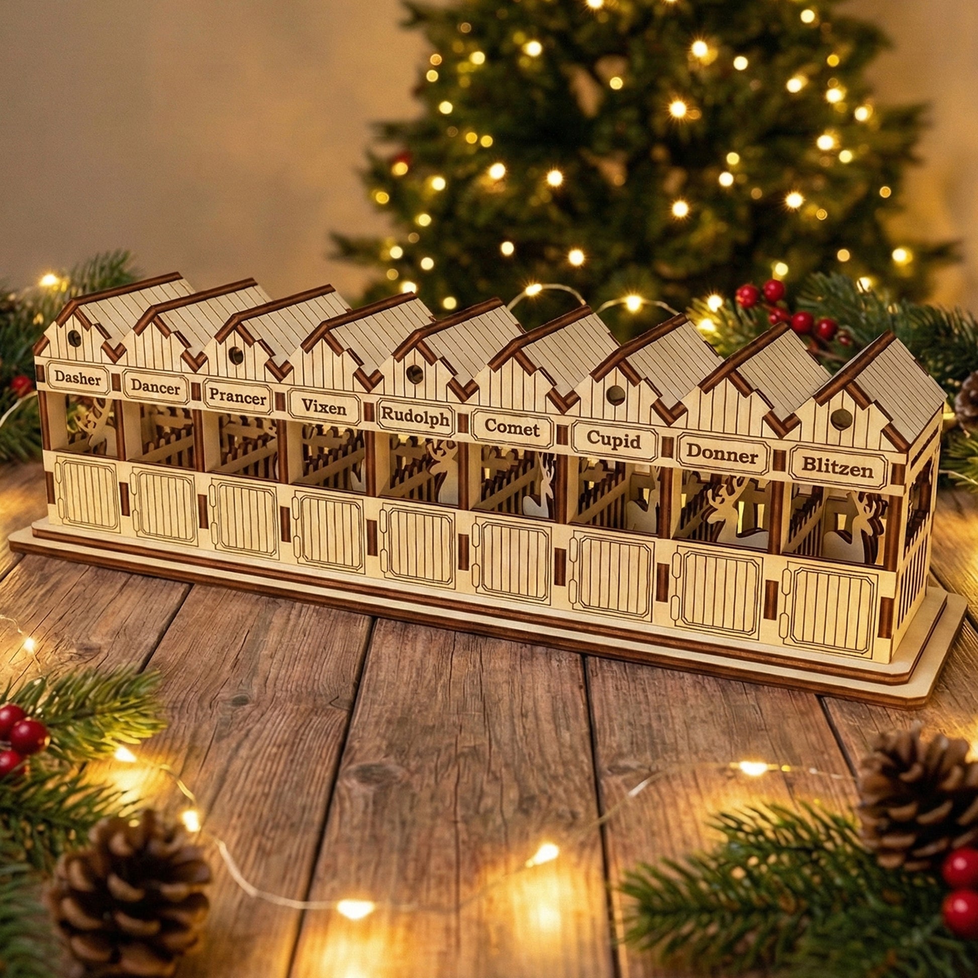 Wooden laser cut Santa's Reindeer stable with nine individual stalls named after Santa's reindeer including Rudolph, illuminated warmly against a softly blurred Christmas tree background.