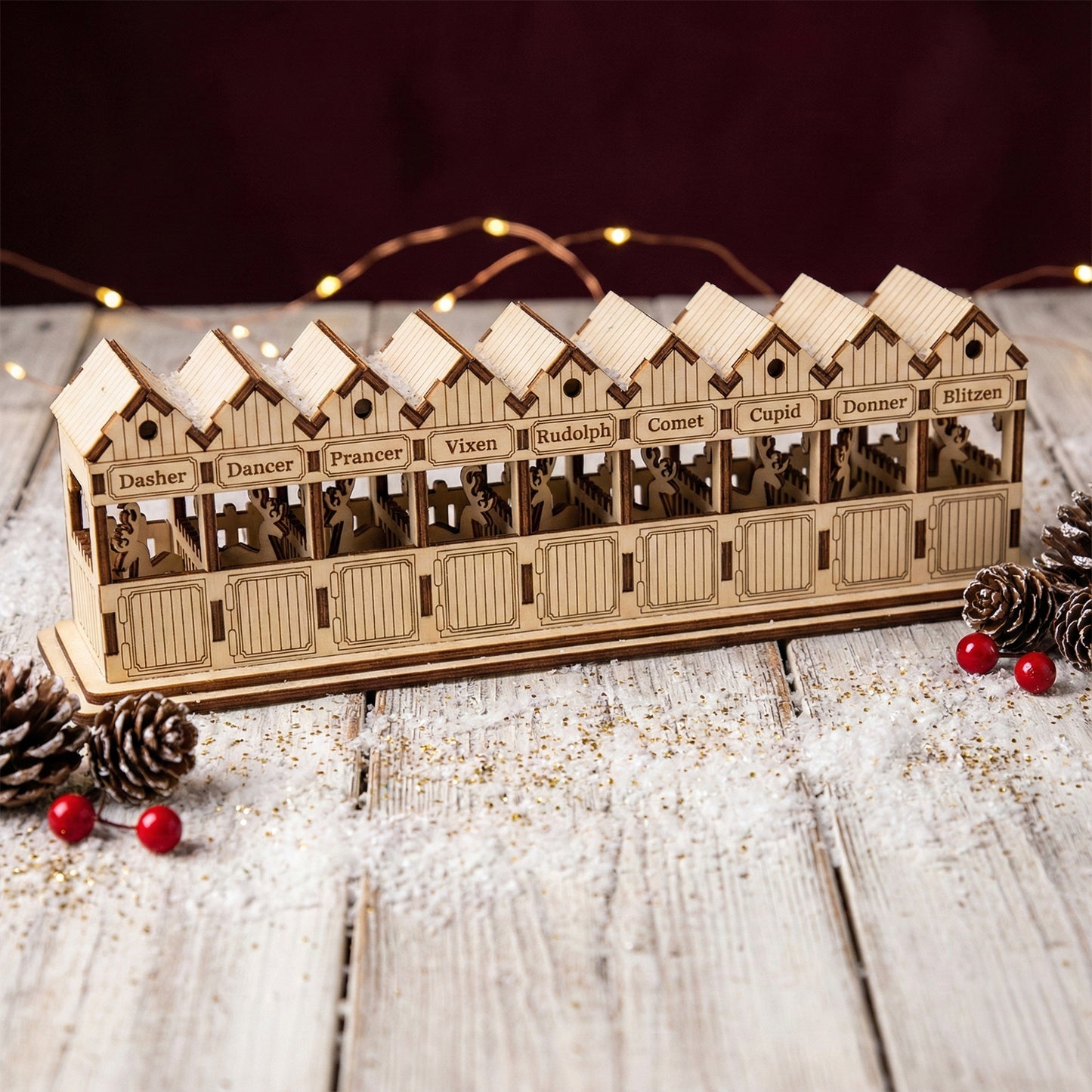 Laser cut wooden Santa's Reindeer stable showing nine cozy stalls with engraved reindeer names and subtle silhouettes, presented against a neutral dark backdrop with festive lights.