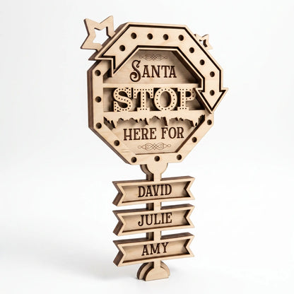Natural unpainted laser cut plywood Santa Stop Here sign with tiered name ribbons, freestanding on a white backdrop.