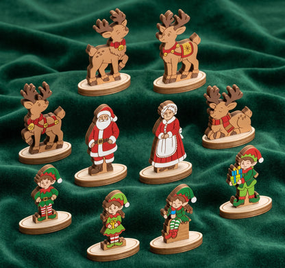 Hand-painted laser cut plywood figurines of Santa, elves, and reindeer on stands over green fabric.