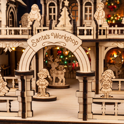Close-up of entrance arch inscribed Santa's Workshop made of laser cut plywood with small elf figure.