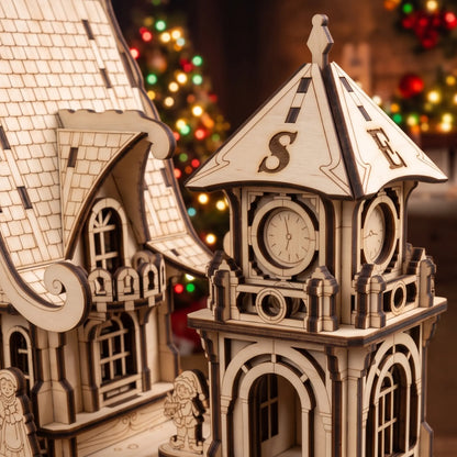 Close-up of laser cut plywood clock tower and carved house facade with glowing Christmas tree bokeh.
