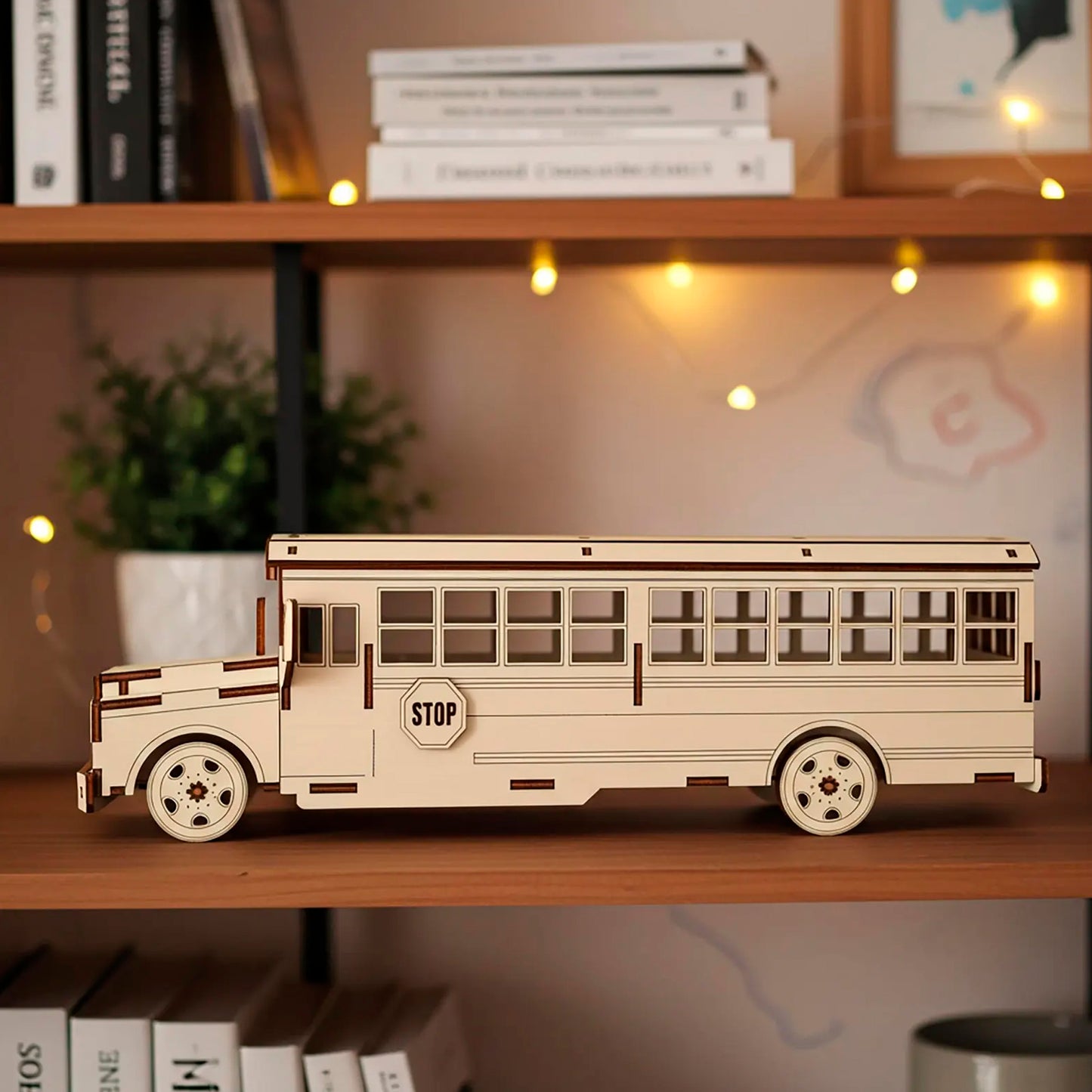 Side profile of a laser cut wooden plywood school bus sitting on a wooden bookshelf. The 3D assembly kit features a side "STOP" sign and multiple window cutouts. Showcases the intricate layers of natural plywood and smooth laser-engraved details.