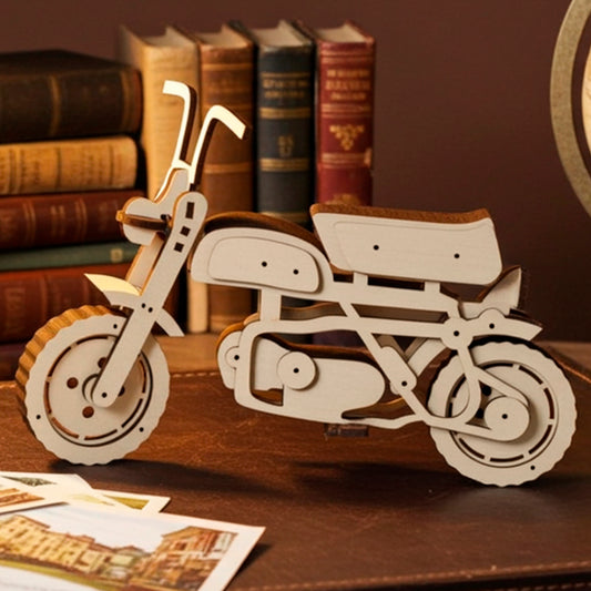 A light wooden plywood laser cut model of a vintage motorcycle or scooter with a dark seat, displayed on a brown leather suitcase, surrounded by old stacked books, an illuminated desk lamp, a globe, and scattered vintage postcards.