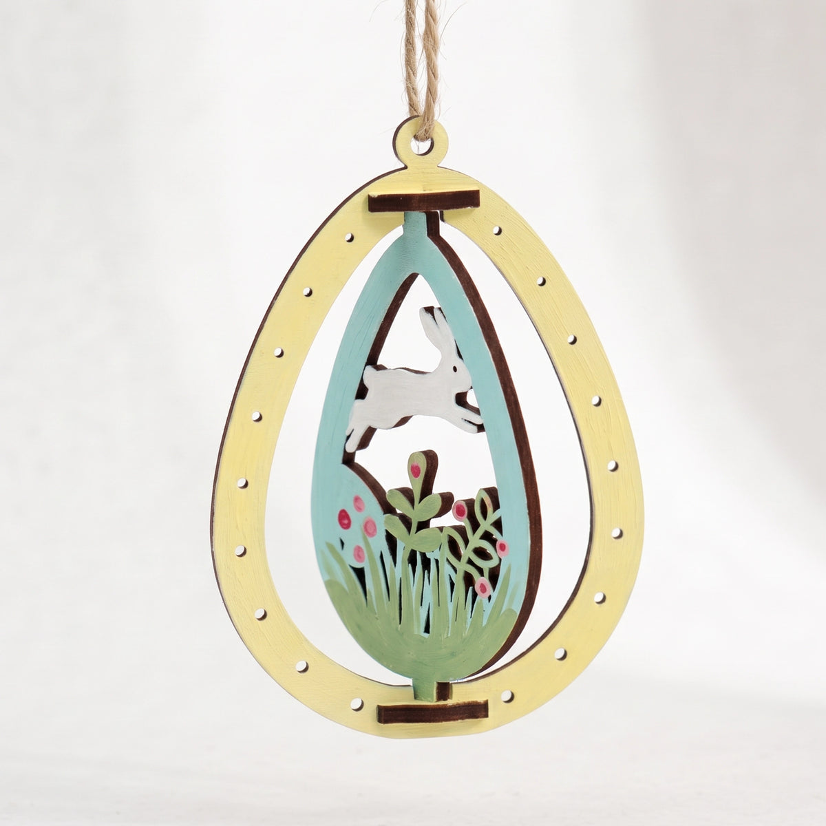 Painted laser cut plywood Easter egg ornament featuring rotating running white bunny in meadow on plain white background.