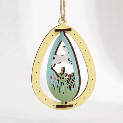Painted laser cut plywood Easter egg ornament featuring rotating running white bunny in meadow on plain white background.