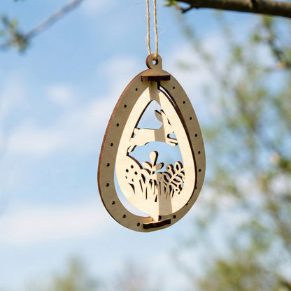 A laser cut plywood Easter egg ornament with a cutout of a rabbit jumping over grass and flowers. The 3D-style wooden frame is suspended by a twine string, showing the smooth wood texture and precise laser-burned details.