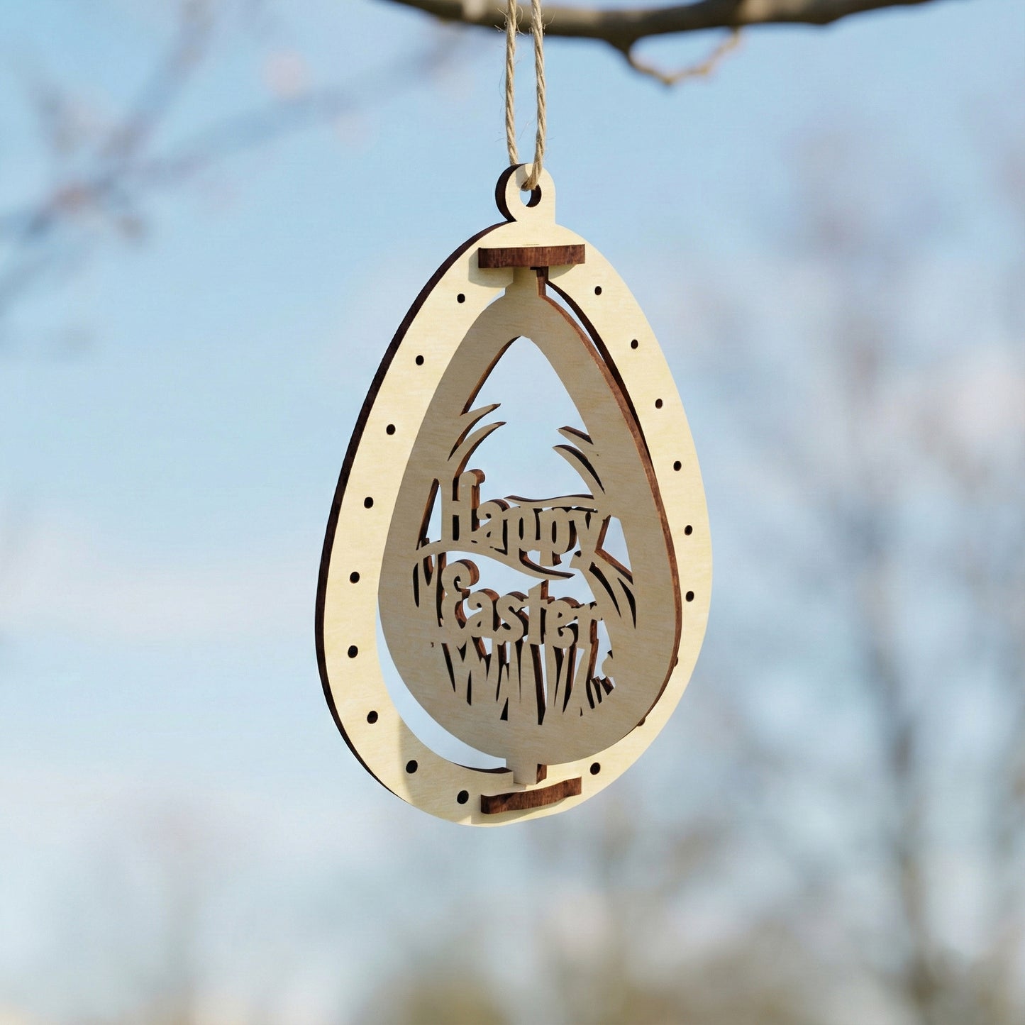 Wooden Easter egg decoration made of laser cut plywood featuring a "Happy Easter" message inside a decorative tall grass silhouette. Hanging from a branch, the ornament highlights clean geometric lines and a warm natural finish.