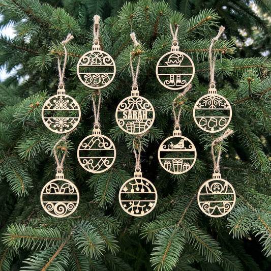 Set of delicate laser cut wooden Name Christmas ornaments featuring custom initials, holiday icons such as gifts and Santa sleighs, displayed suspended from branches on a lush Christmas tree background.