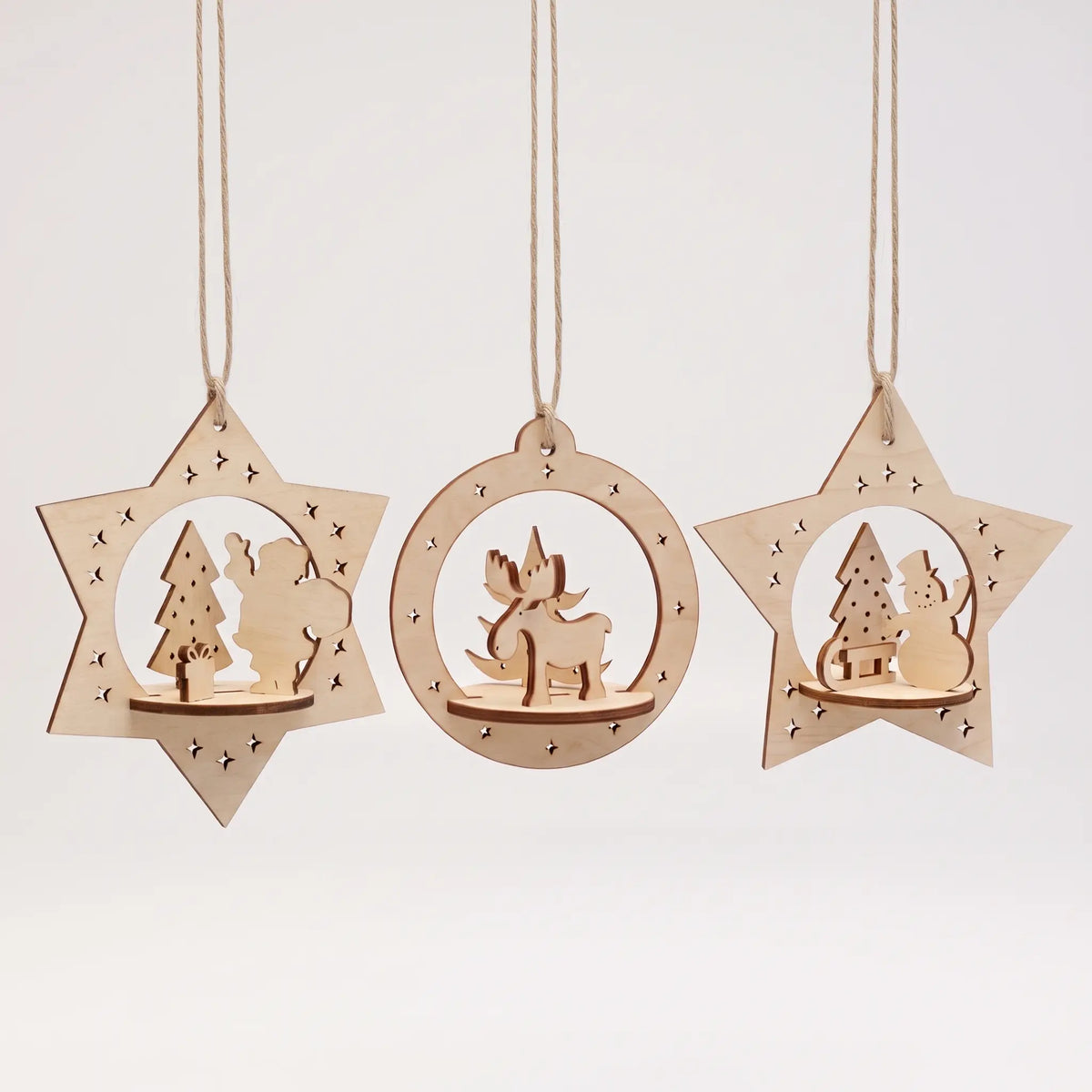Set of three hanging laser cut plywood Christmas ornaments with cute festive scenes on white backdrop.