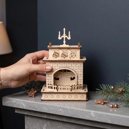 Hand arranges laser cut plywood fireplace mantel with Santa legs and candelabra on marble shelf with pine sprigs.