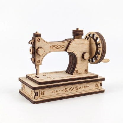 A miniature laser cut sewing machine model with a hand-crank design, crafted from light and dark natural wood with laser-engraved details, shown on a clean white background.