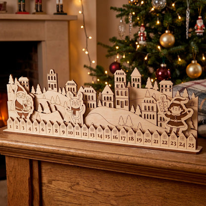 A laser cut plywood  advent calendar with a winter scene and a small Christmas tree in the background.