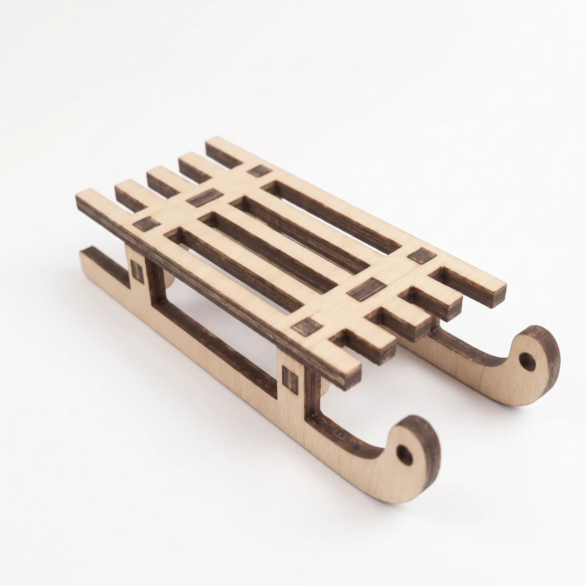 Side perspective view of a miniature laser cut plywood winter sled model isolated on a white background.