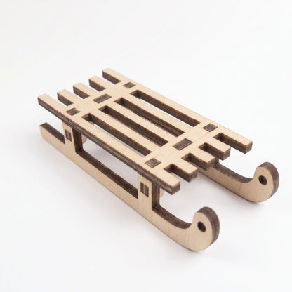 Side perspective view of a miniature laser cut plywood winter sled model isolated on a white background.