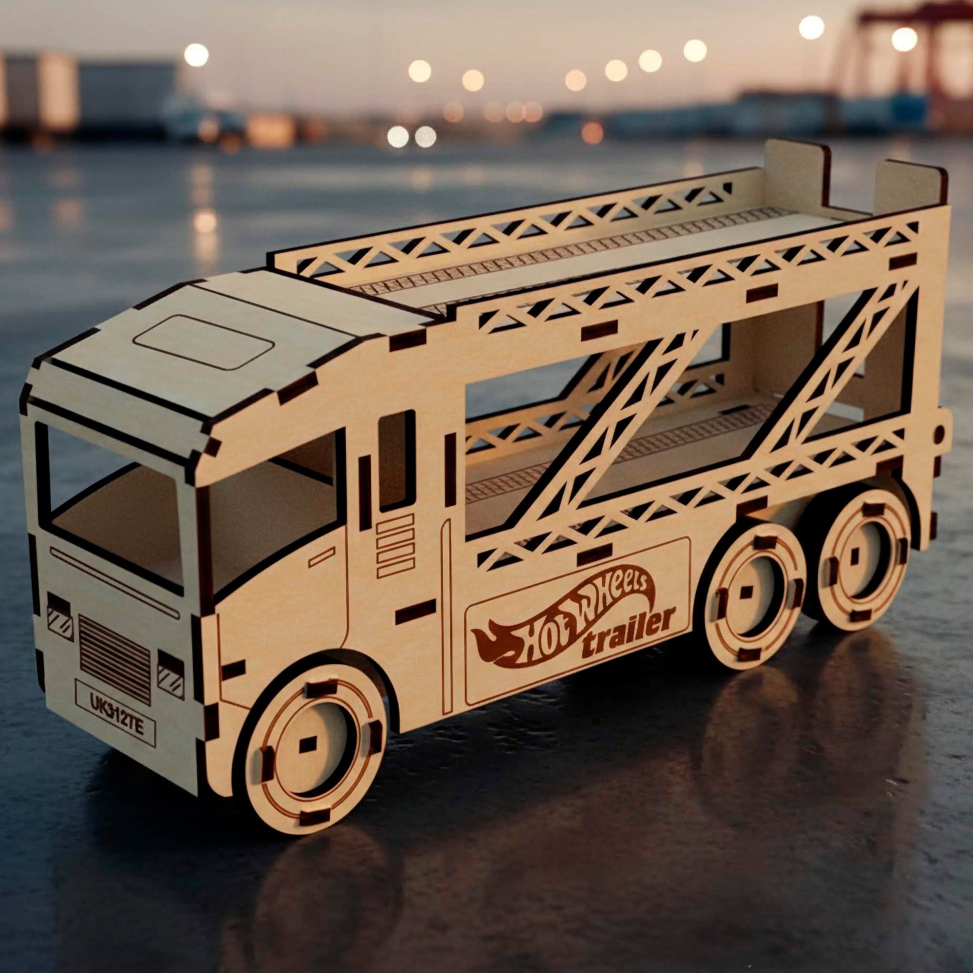 High-angle front view of a laser cut wooden plywood car hauler truck. The plywood model features a double-decker trailer for small cars, engraved "Hot Wheels trailer" logo, set against a sunset port background.