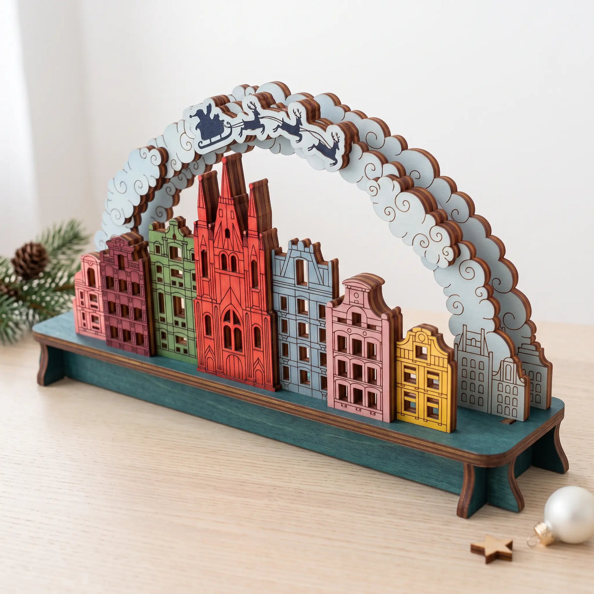 Colorful painted laser cut plywood Christmas city arch with cathedral, townhouses, and Santa sleigh on curved cloud arch.