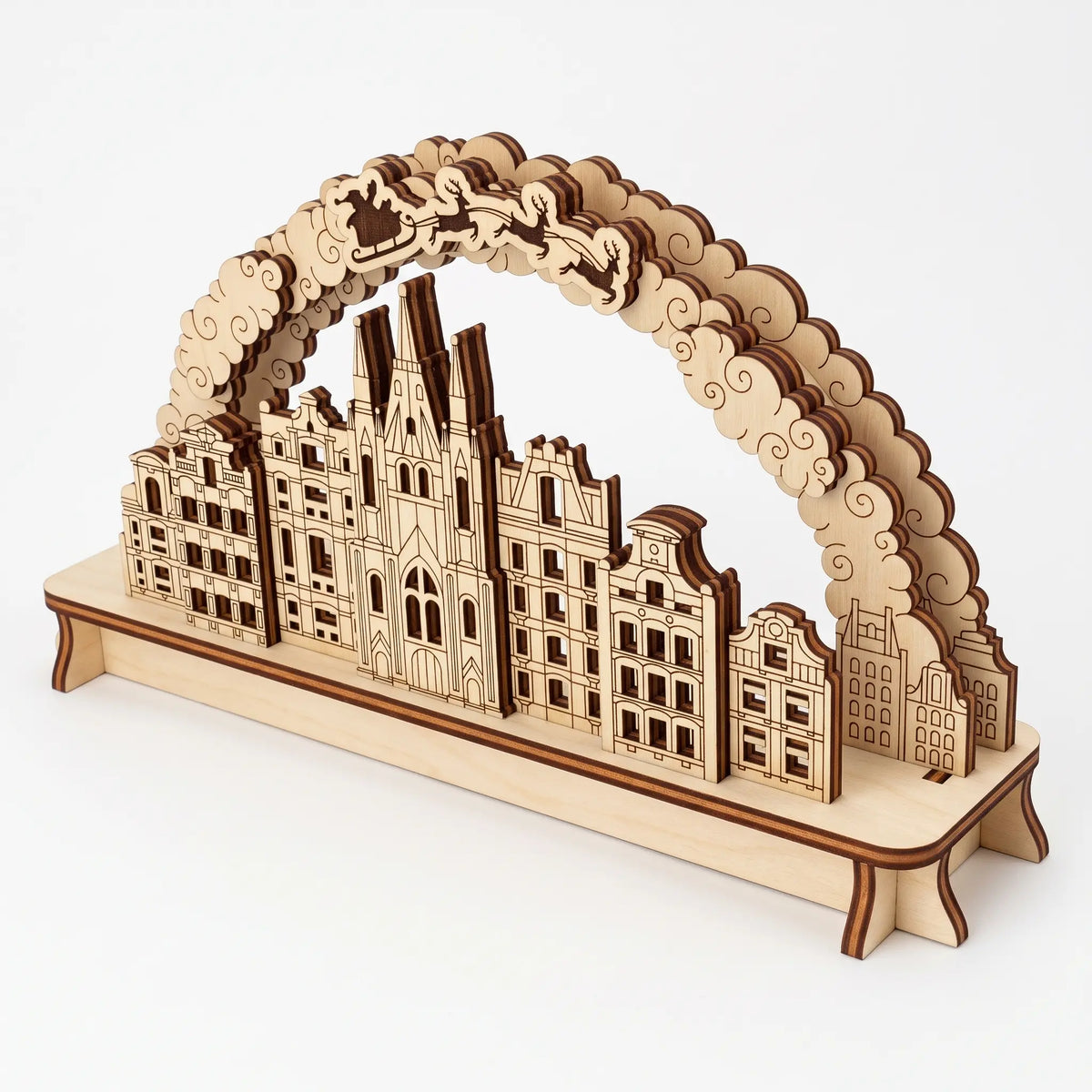 High angle view of wooden laser cut plywood Christmas city arch with layered townhouses and Santa sleigh on white backdrop.