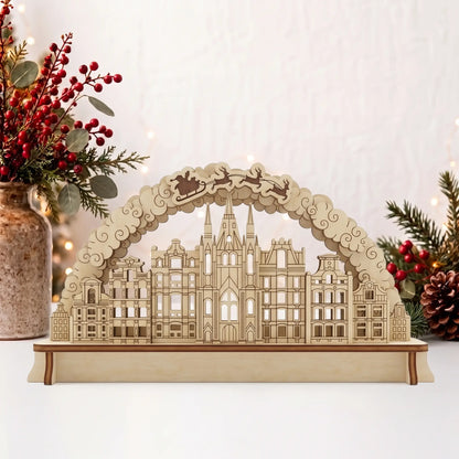 Laser cut plywood Christmas city arch diorama on table beside vase of red berries, pine branches, and holiday fairy lights.