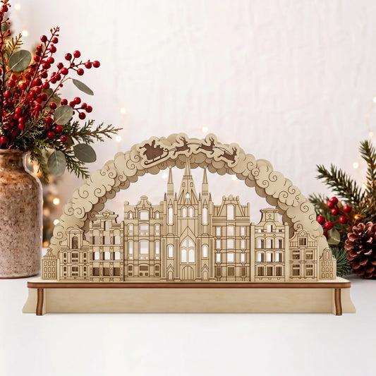 Laser cut plywood Christmas city arch diorama on table beside vase of red berries, pine branches, and holiday fairy lights.