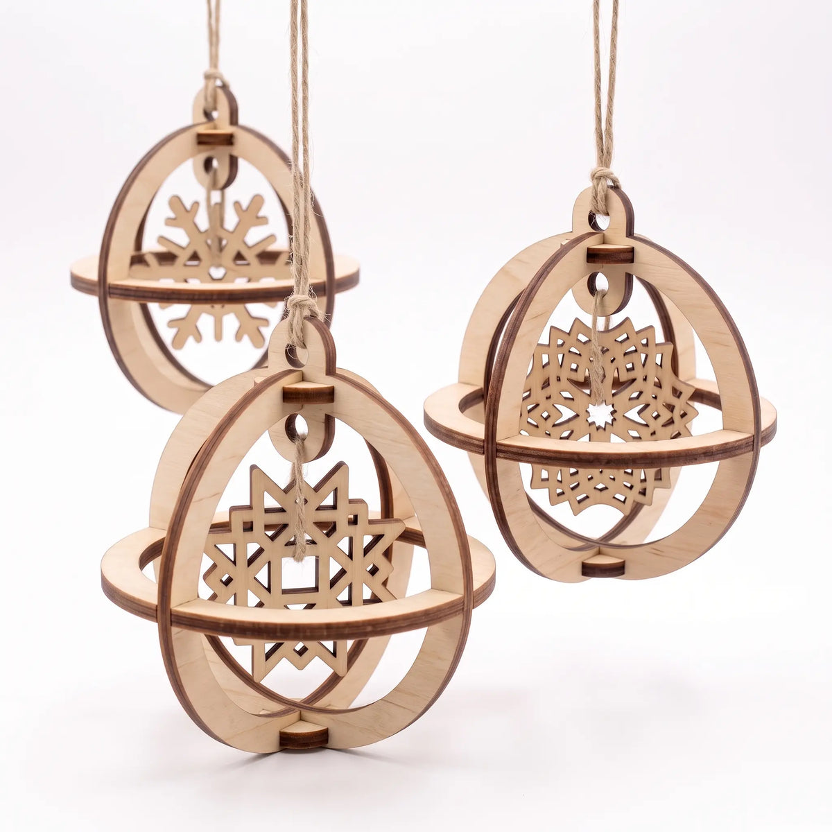 Trio of 3D laser cut plywood spherical baubles with suspended internal snowflakes hanging against white.