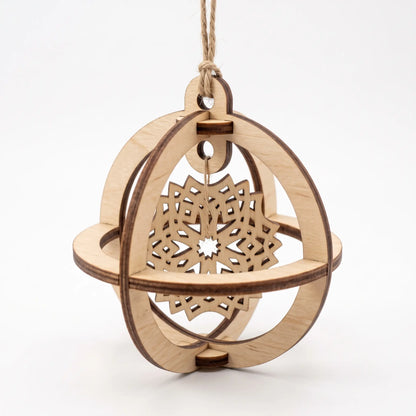 Front-angle view of 3D laser cut plywood sphere bauble with suspended layered snowflake motif on white.