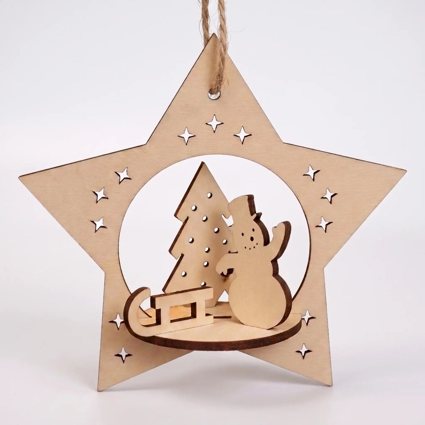 Front view of laser cut plywood star ornament with 3D miniature snowman, sled, and tree, hanging against white base.
