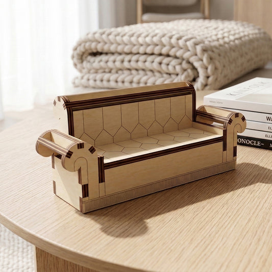 Detailed side angle of a miniature laser cut plywood couch. Highlights the layered wood construction, scrolled arms, and hexagonal patterns etched into the cushions. A chunky knit blanket and books are blurred in the background.