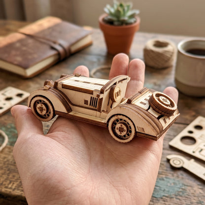 A hand holding a miniature vintage sport car model crafted from laser cut plywood, showing its compact size.