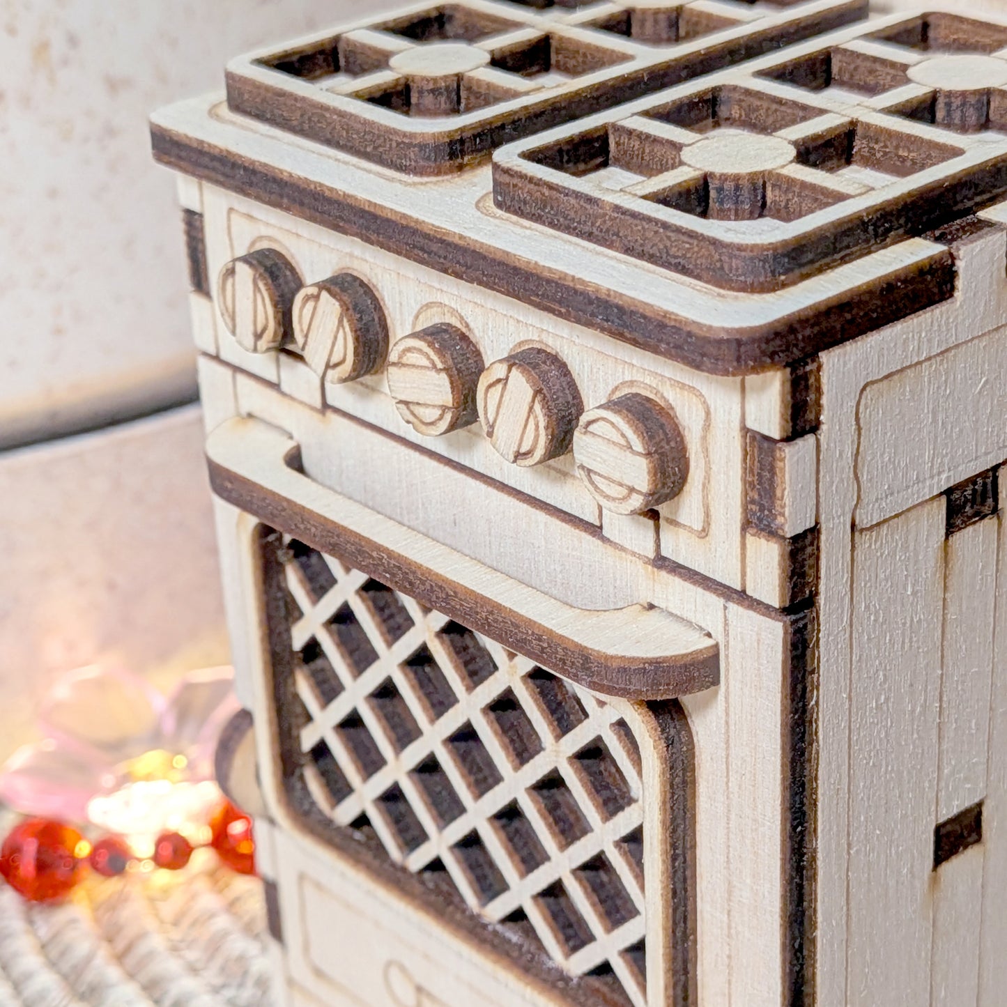 Close-up of a laser cut wooden miniature stove highlighting engraved knobs, layered oven handle, and lattice oven door