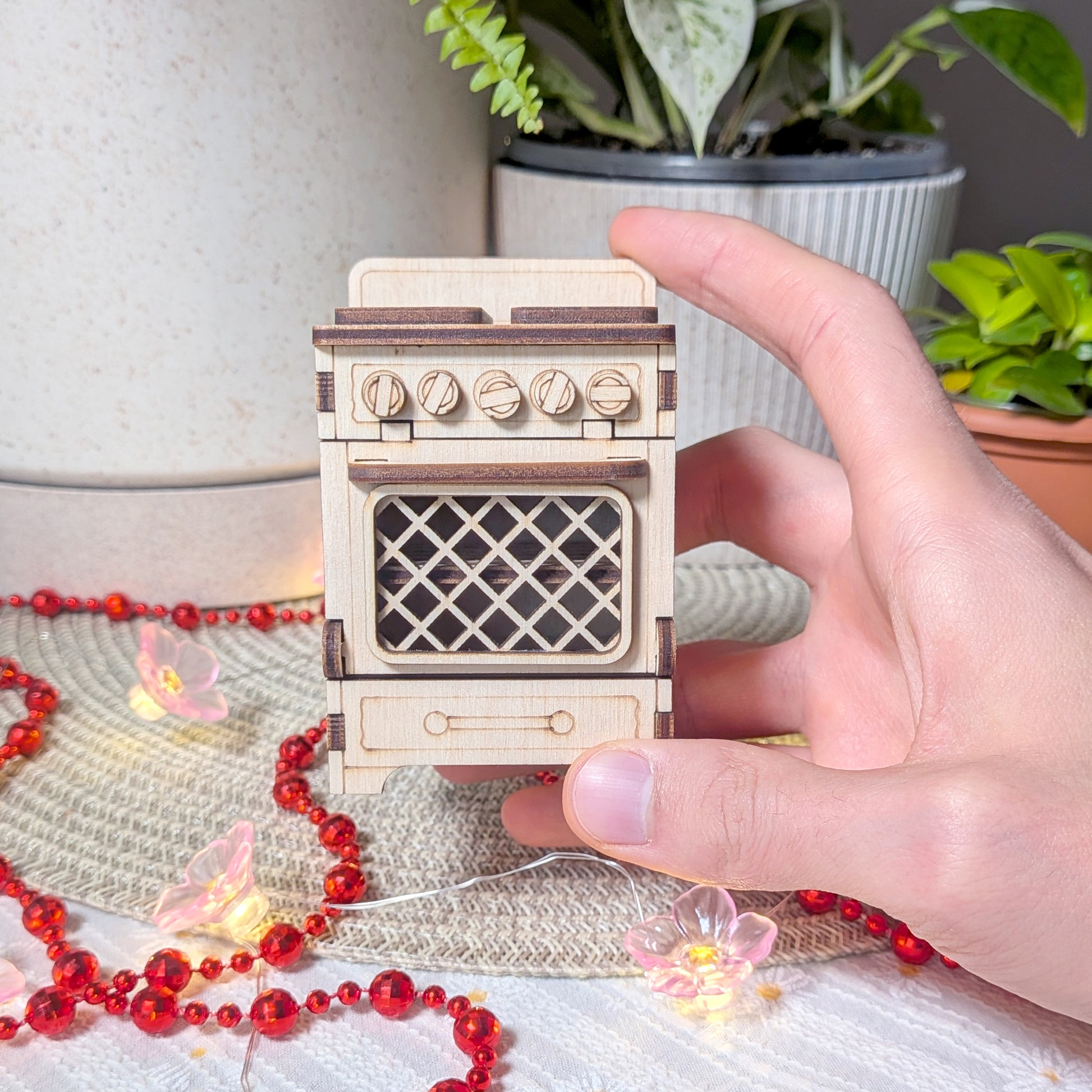 Laser cut wooden dollhouse stove held in a hand, featuring engraved knobs, a lattice oven door, and detailed plywood construction