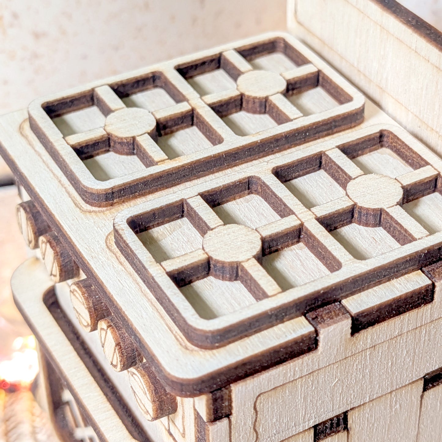Close-up of a laser cut wooden miniature stove showing four detailed burner grates made from layered light and dark plywood.