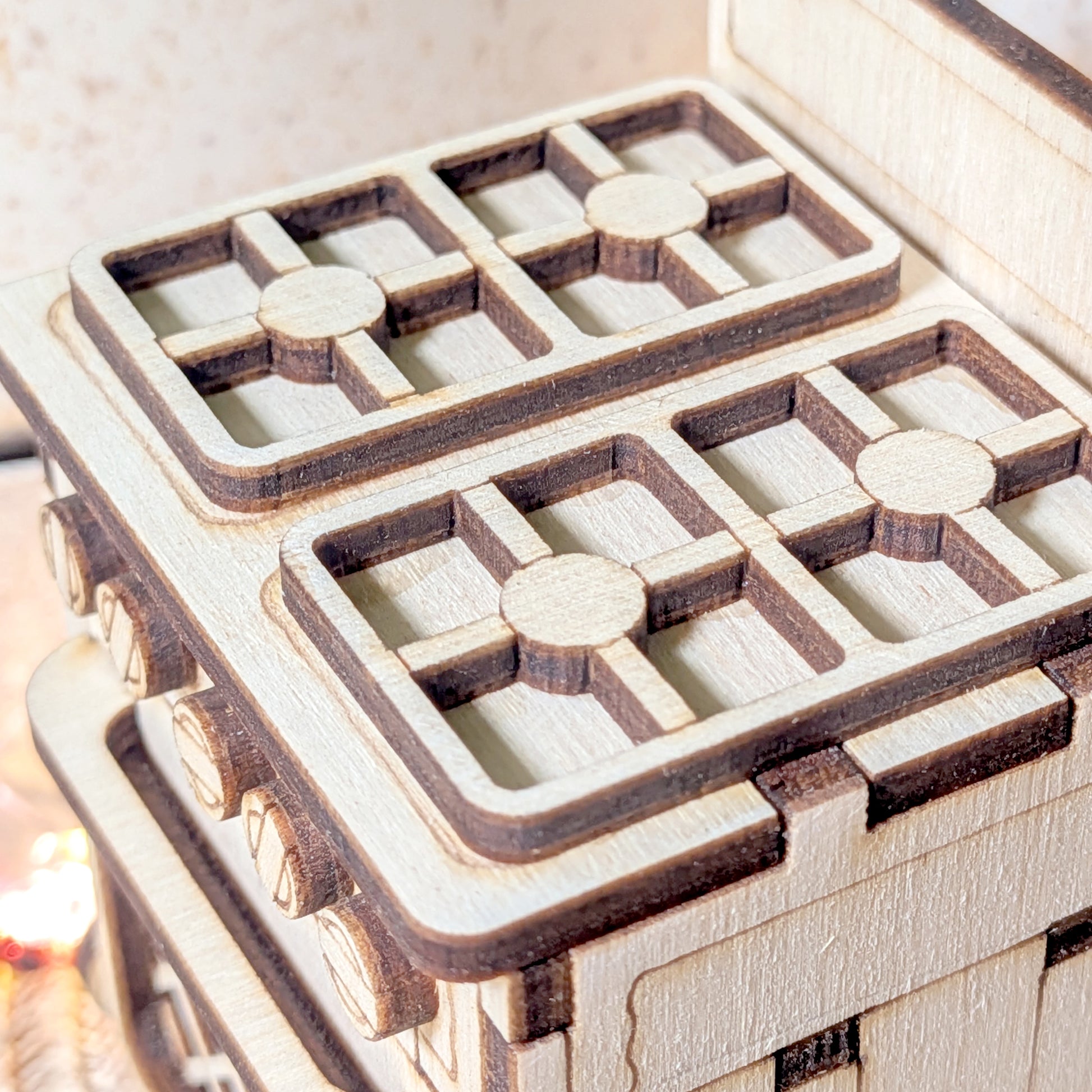 Close-up of a laser cut wooden miniature stove showing four detailed burner grates made from layered light and dark plywood.
