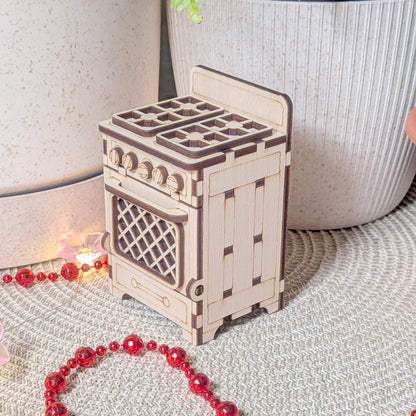 Laser cut wooden dollhouse stove displayed on a textured mat, showing detailed knobs, burners, and lattice oven door