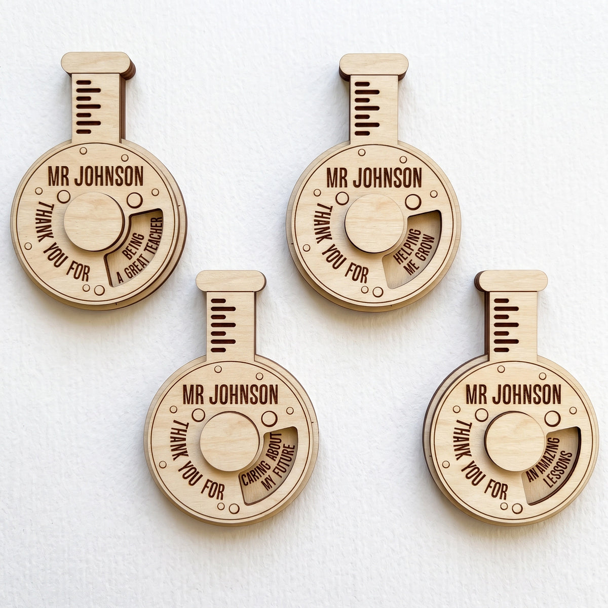 Four laser cut plywood science flask teacher gifts with spinning wheels showing thank you messages on plain white background.