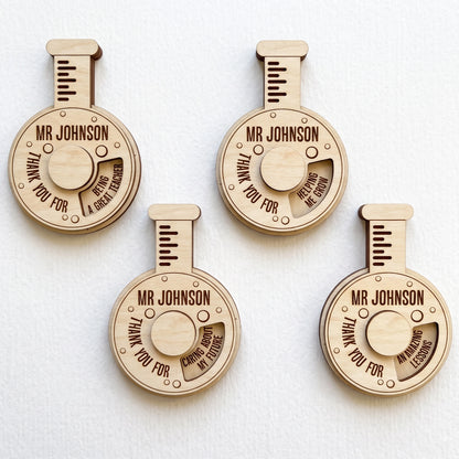 Four laser cut plywood science flask teacher gifts with spinning wheels showing thank you messages on plain white background.