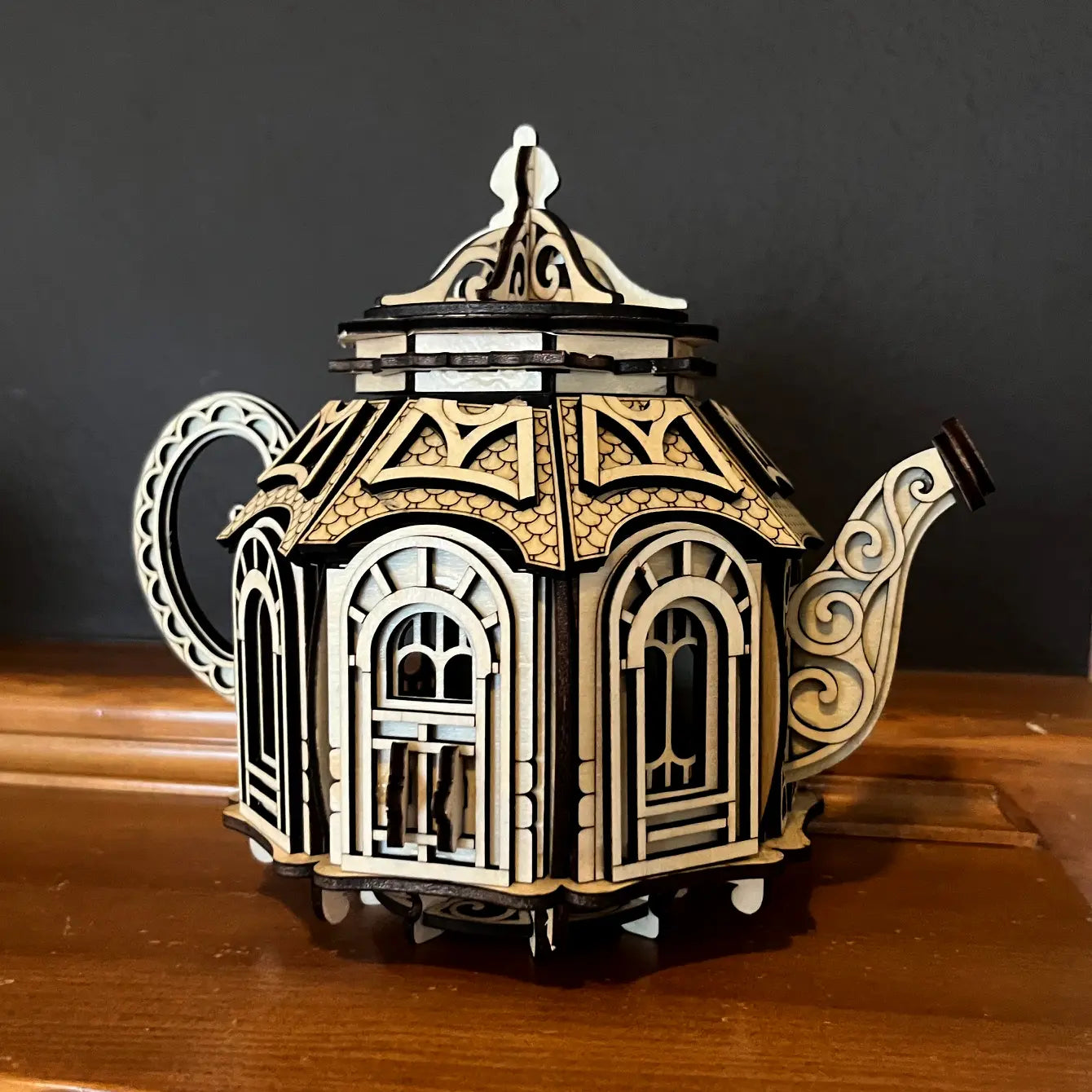 An assembled laser cut plywood teapot fairy house model showing layered arched windows against a dark background.