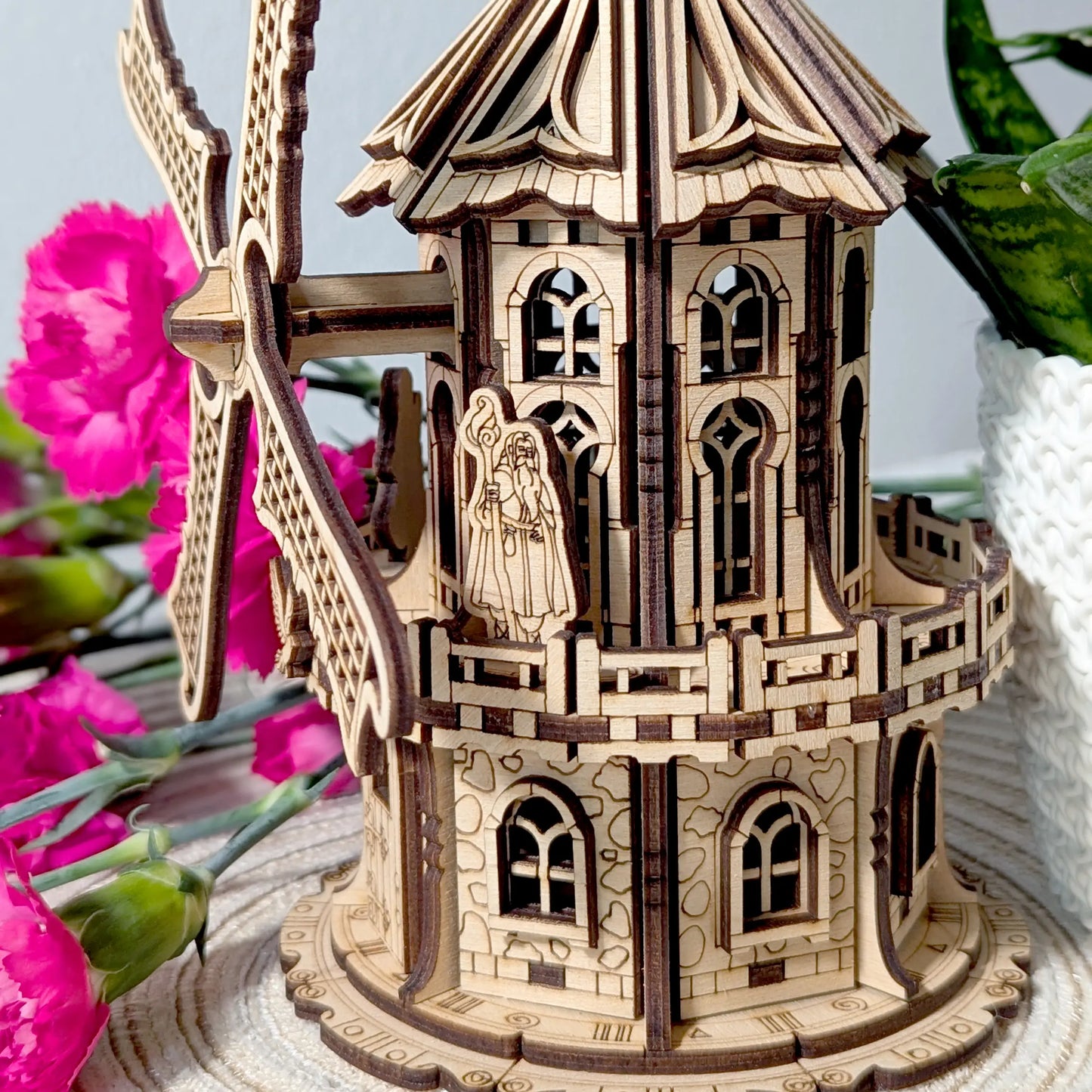 Macro close-up shot of a small wizard figurine standing on the balcony of a detailed laser cut plywood windmill model.