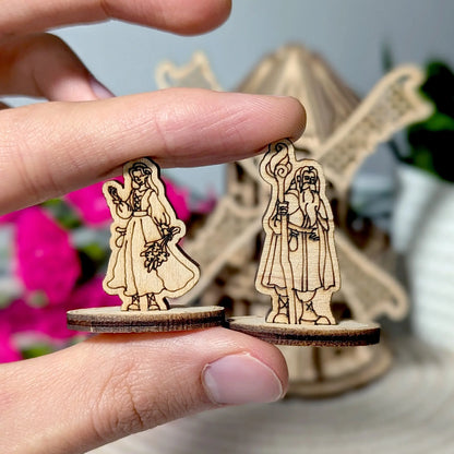 Fingers holding up two small character standees to clearly show the scale of the laser cut plywood model accessories.