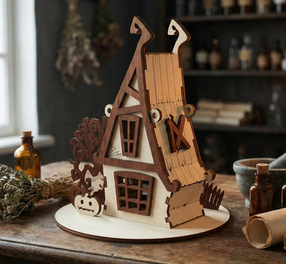 Side perspective of the miniature witch's house showing the interlocking laser cut plywood joints. A large window with a dark wood frame is visible on the lower floor. The house is set against a background of blurred herbalist jars.