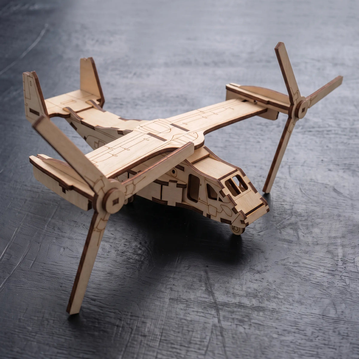 High-angle view of 3D laser cut plywood tiltrotor aircraft model with dual rotatable prop-rotors on dark textured surface.