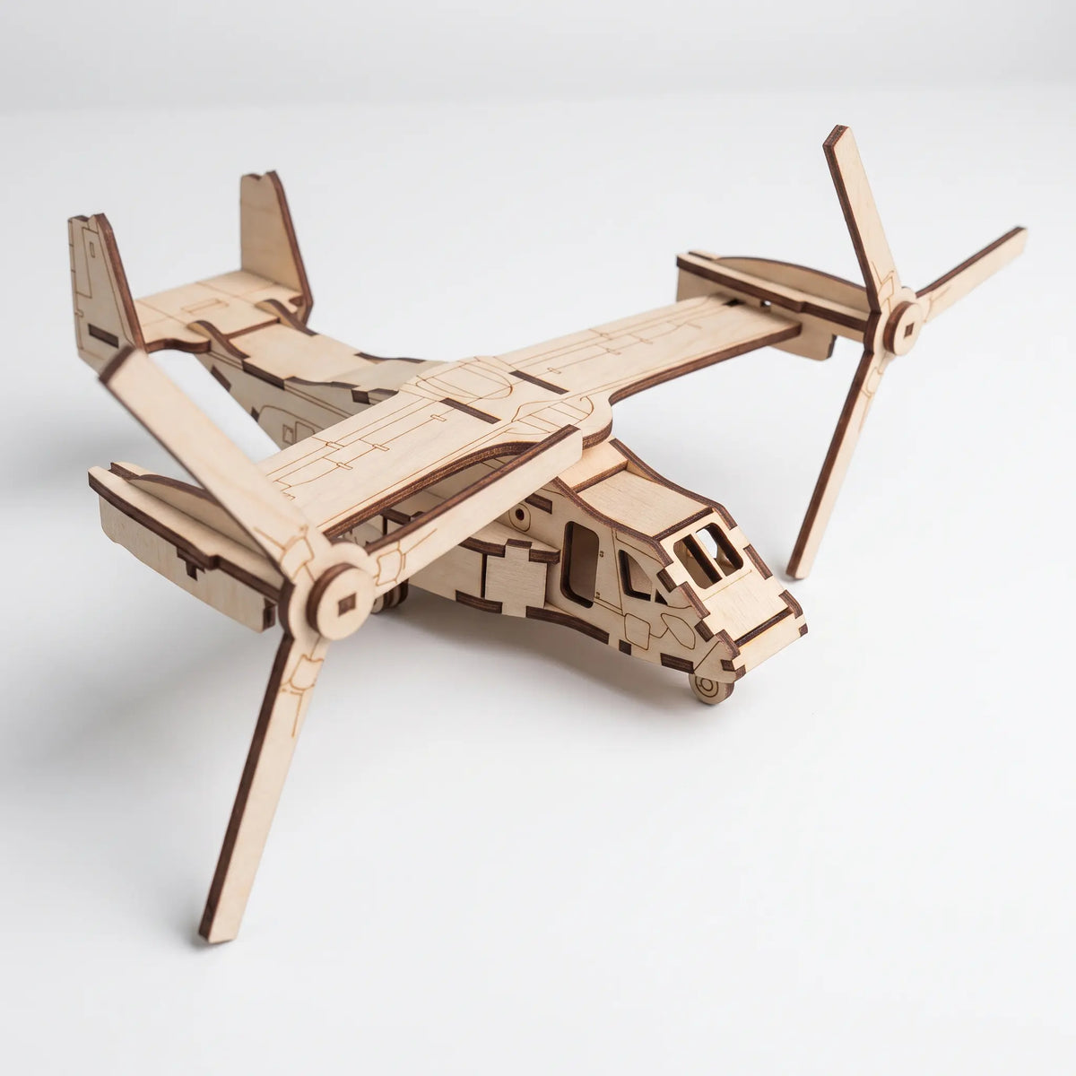 Front angle view of 3D laser cut plywood tiltrotor aircraft model showing cockpit, fuselage, and rotors on white background.