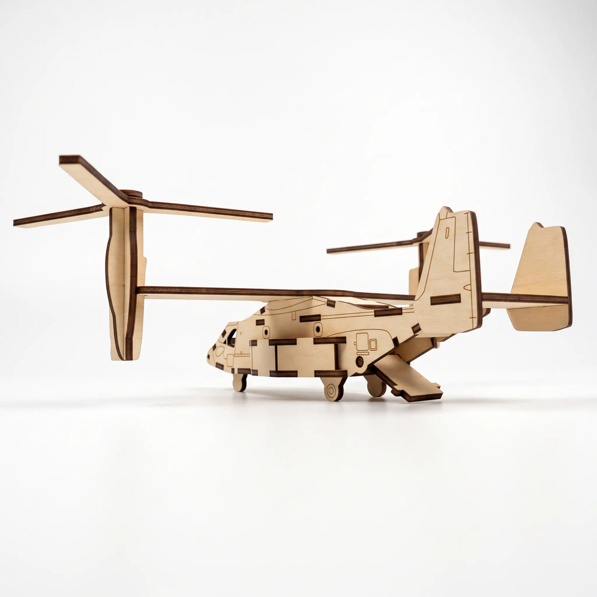 Rear side view of 3D laser cut plywood tiltrotor aircraft model with open cargo ramp and tail fins on plain white background.