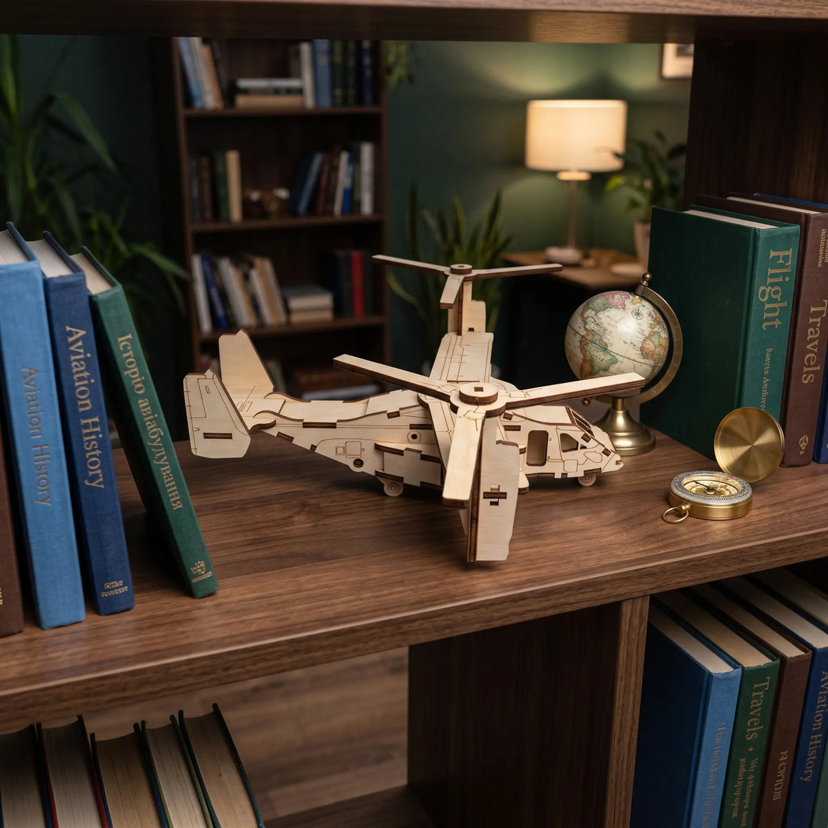 Laser cut plywood tiltrotor aircraft model standing on wooden bookshelf beside aviation history books, globe, and compass.