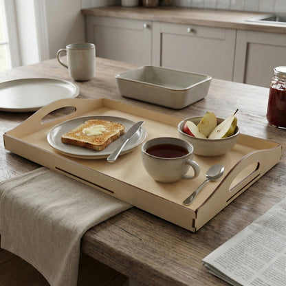 Untreated wood laser cut tray with ergonomic handles, carrying buttered toast, fresh fruit slices, and tea, placed on a rustic kitchen table background.